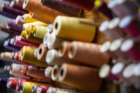 image of multiple spools of thread in various colors, including yellow, orange, purple, pink, and brown, arranged on a rack
